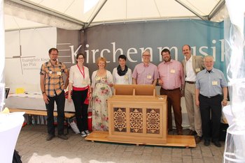 Kirchenmusik Fröhliche katholische und evangelische Kirchenmusiker stehen in einem Pavillon hinter einer Truhenorgel.